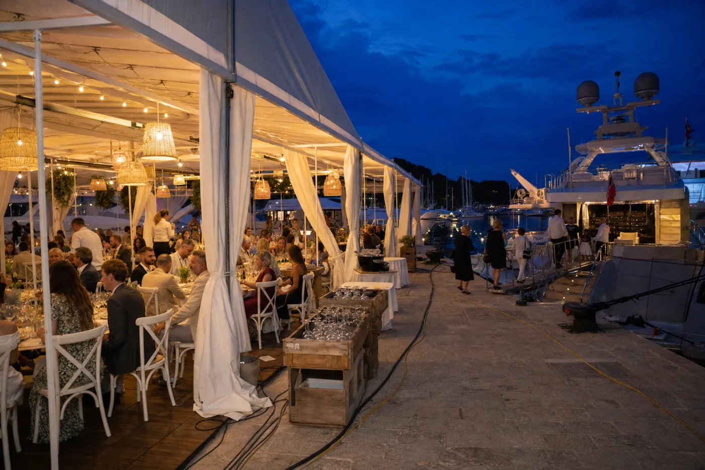 A dressed marquee on a harbour quay at dusk beside moored yachts